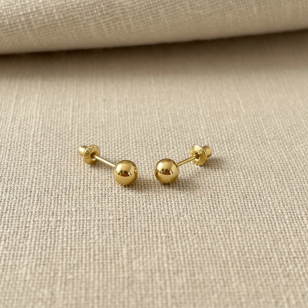 Gold ball stud earrings on beige linen background
