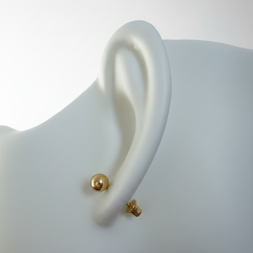 Gold ball stud earring on white ceramic ear display